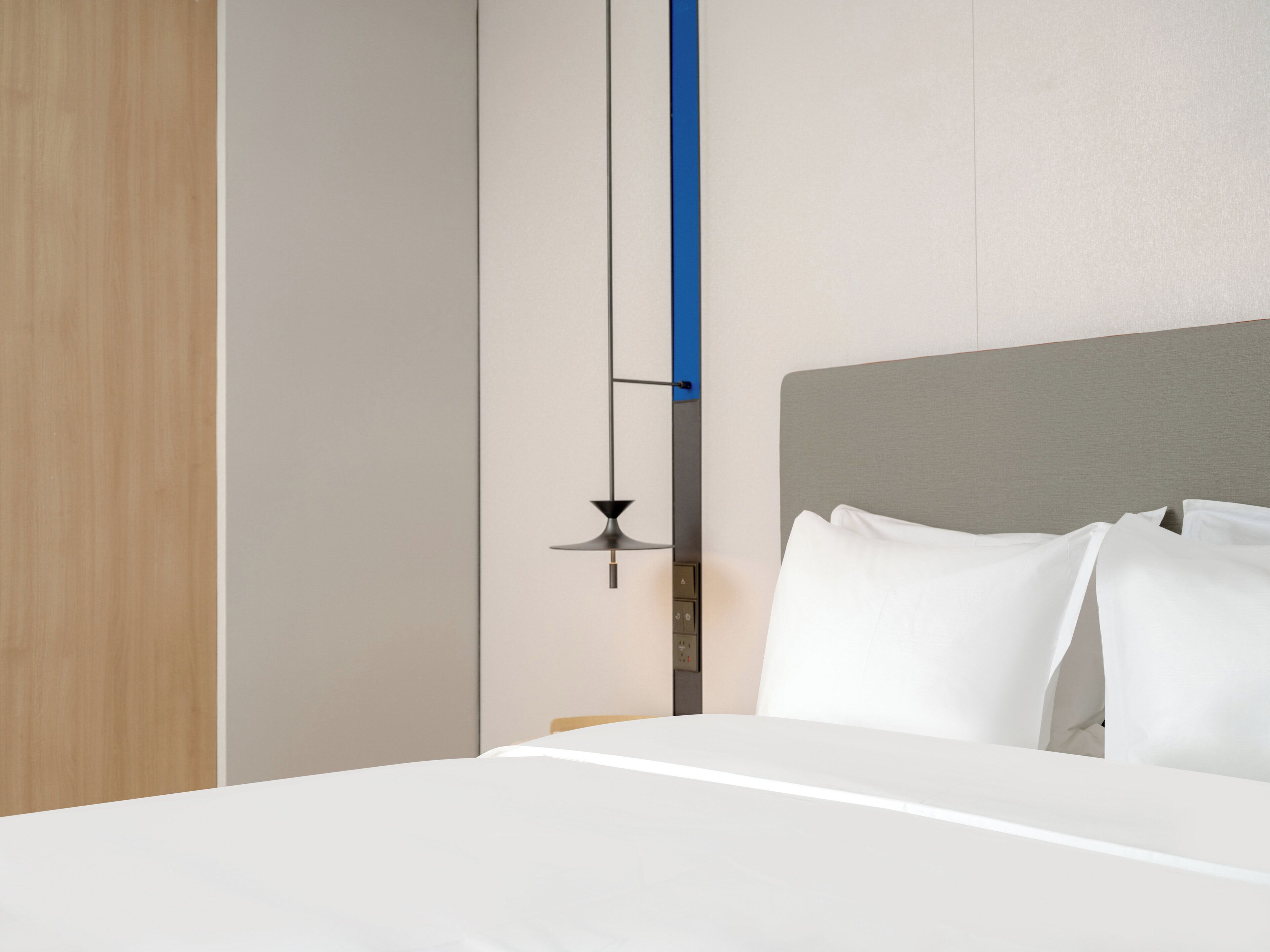 A modern hotel room with a neatly made bed, a wall-mounted light fixture, and a wooden door.