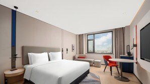 Una habitación de hotel moderna con una cama grande, un escritorio, una silla y vistas de la ciudad a través de la ventana.