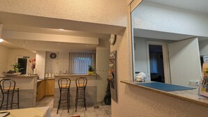 Una cocina moderna con una isla central, taburetes de bar y un comedor con vista al salón.