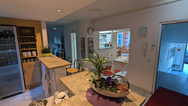 Una cocina con refrigerador, estantes con botellas, un lavamanos y un comedor con sillas y una mesa.