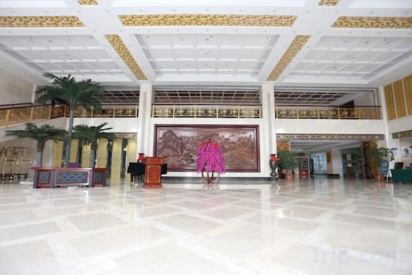 Een ruime lobby met een hoge plafond, een groot muurschildering en een trap naar een hoger niveau.