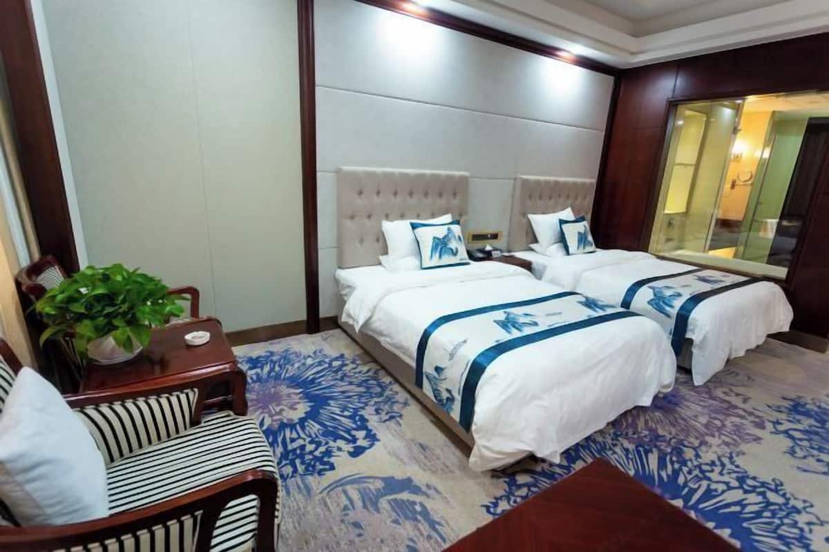 Une chambre d’hôtel avec deux lits, un canapé, une petite table et une plante en pot.