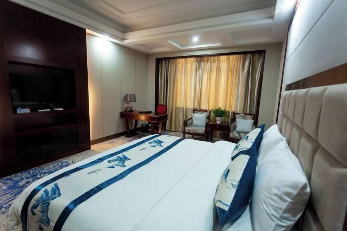 Une chambre d’hôtel avec un grand lit, une télévision, un bureau avec une lampe, une chaise et une fenêtre avec des rideaux.