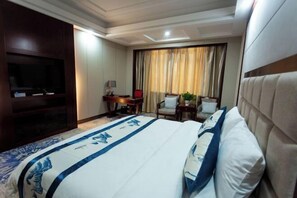 A hotel room with a large bed, a television, a desk with a lamp, a chair, and a window with curtains. - Guoyuan Hotel (Taizhou)