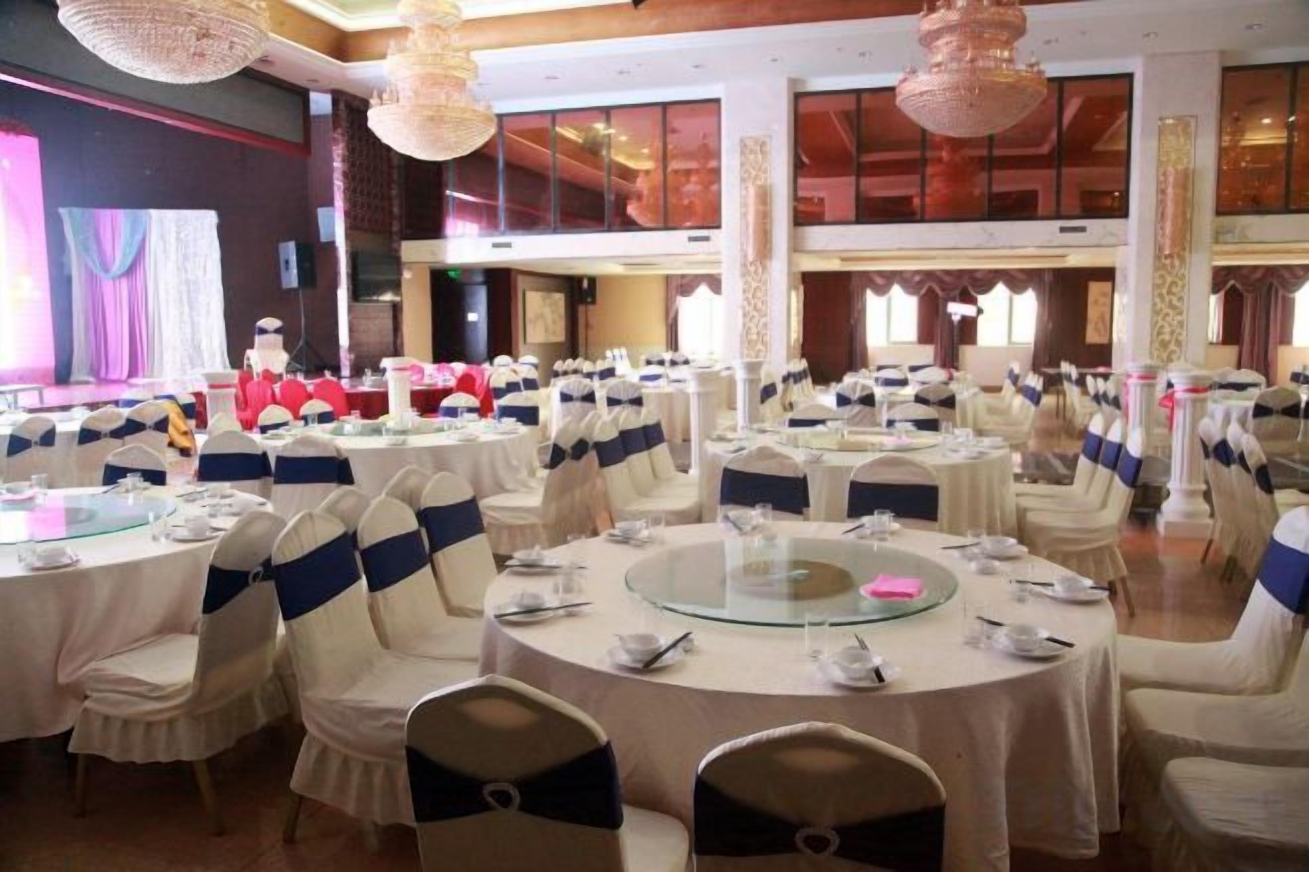 A banquet hall with round tables, chairs, and a stage with a red backdrop.