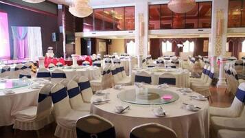 A banquet hall with round tables, chairs, and a stage with a red backdrop.