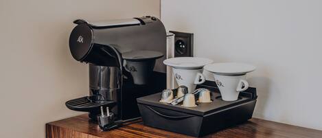 A coffee maker with two cups on a wooden table.