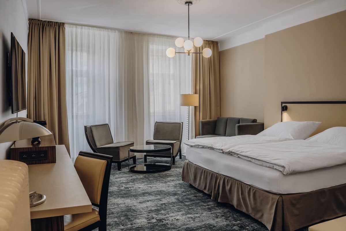 A hotel room with a bed, a desk, a chair, a small table, and a TV.