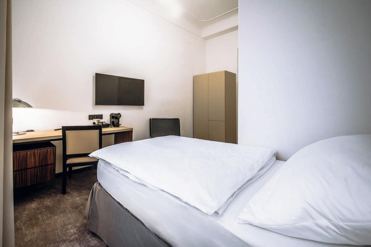 A hotel room with a bed, a desk, a chair, a television, and a wardrobe.