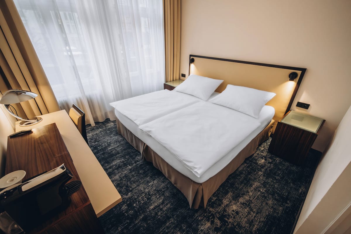 A hotel room with a large bed, a desk with a lamp, and a window with curtains.