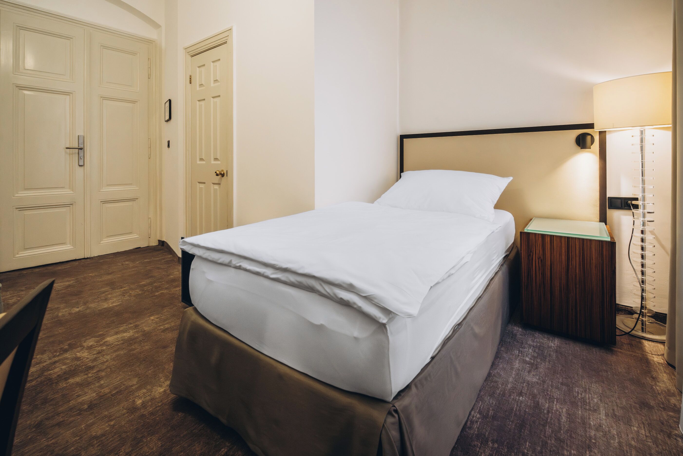 A hotel room with a bed, a nightstand, a lamp, and a wardrobe.