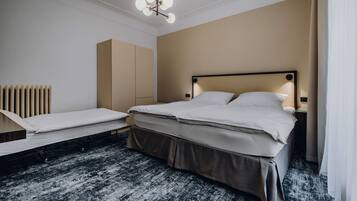 Ett modernt hotellrum med en stor säng, en mindre säng, ett sängbord, en lampa och ett element.