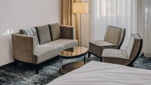 Una habitación de hotel con una cama, un sofá, una silla, una mesita y una lámpara de pie.