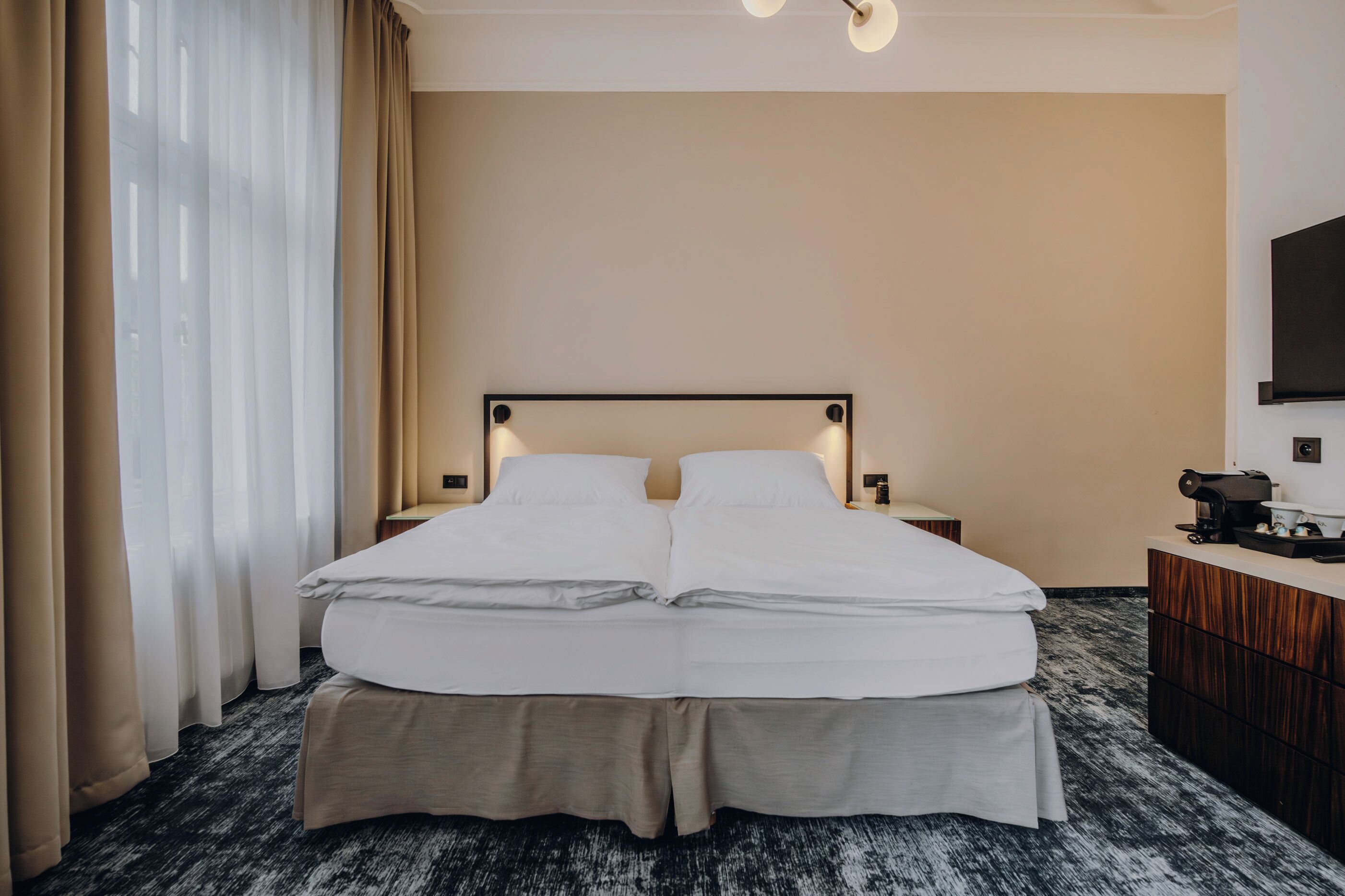 Een hotelkamer met een tweepersoonsbed, een bureau met stoel, een flatscreen televisie aan de muur en een raam met gordijnen.