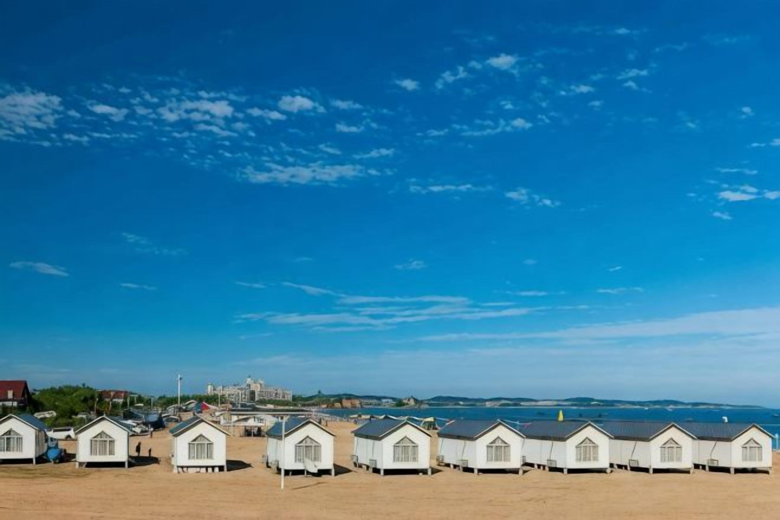 Una hilera de cabañas de playa con vista despejada al mar y un edificio distante.