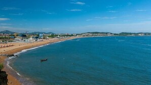 A coastal view with a beach, ocean, and distant buildings. - Dalian Mong Kok Express Hotel (Dalian)