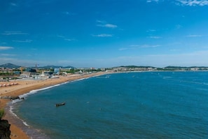 Vista costera con playa, océano y edificios a lo lejos.