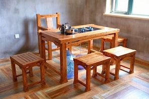 Una mesa de madera para comer con cuatro sillas, una tetera y un florero azul sobre la mesa.