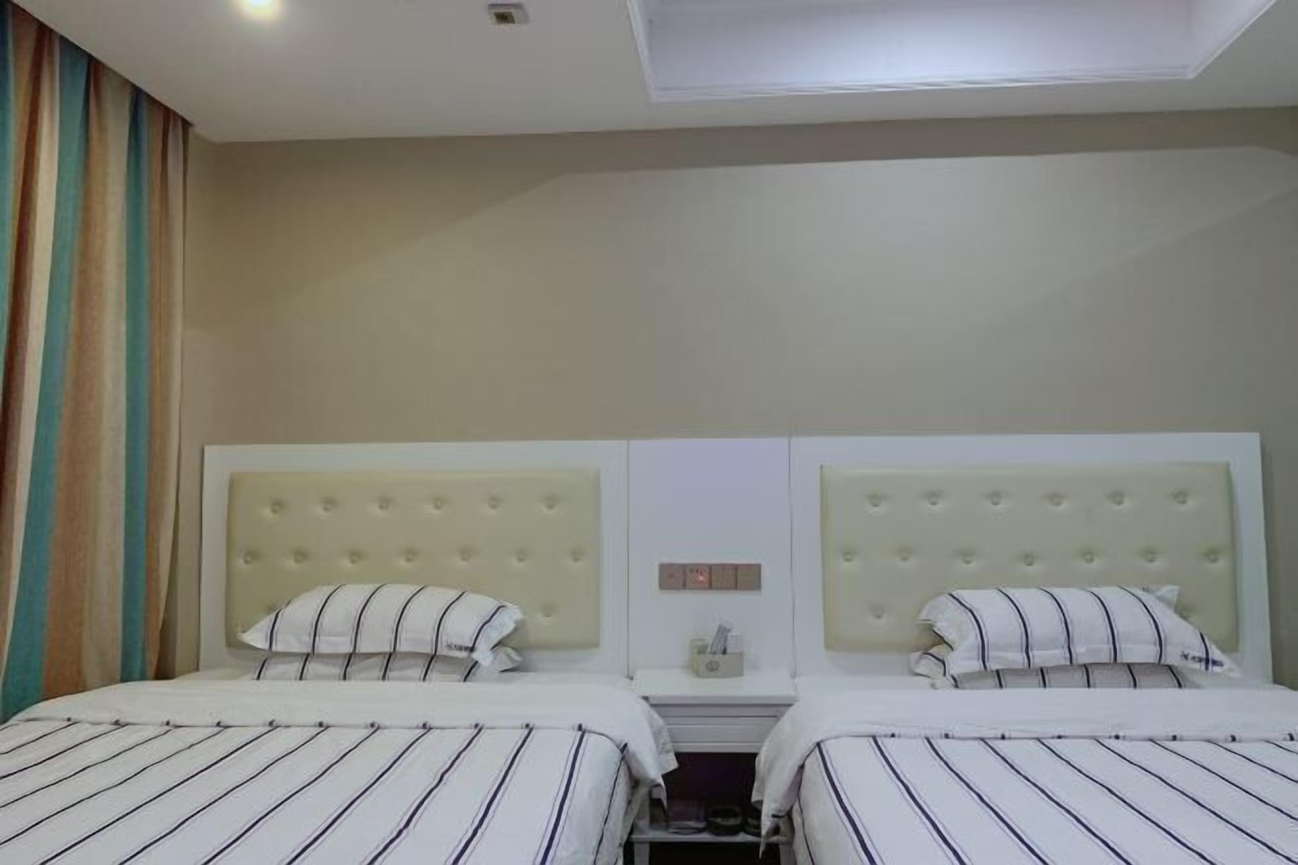 Habitación de hotel con dos camas, cada una con ropa de cama a rayas y un cabecero capitonado.