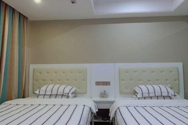 Habitación de hotel con dos camas, cada una con ropa de cama a rayas y un cabecero capitonado.