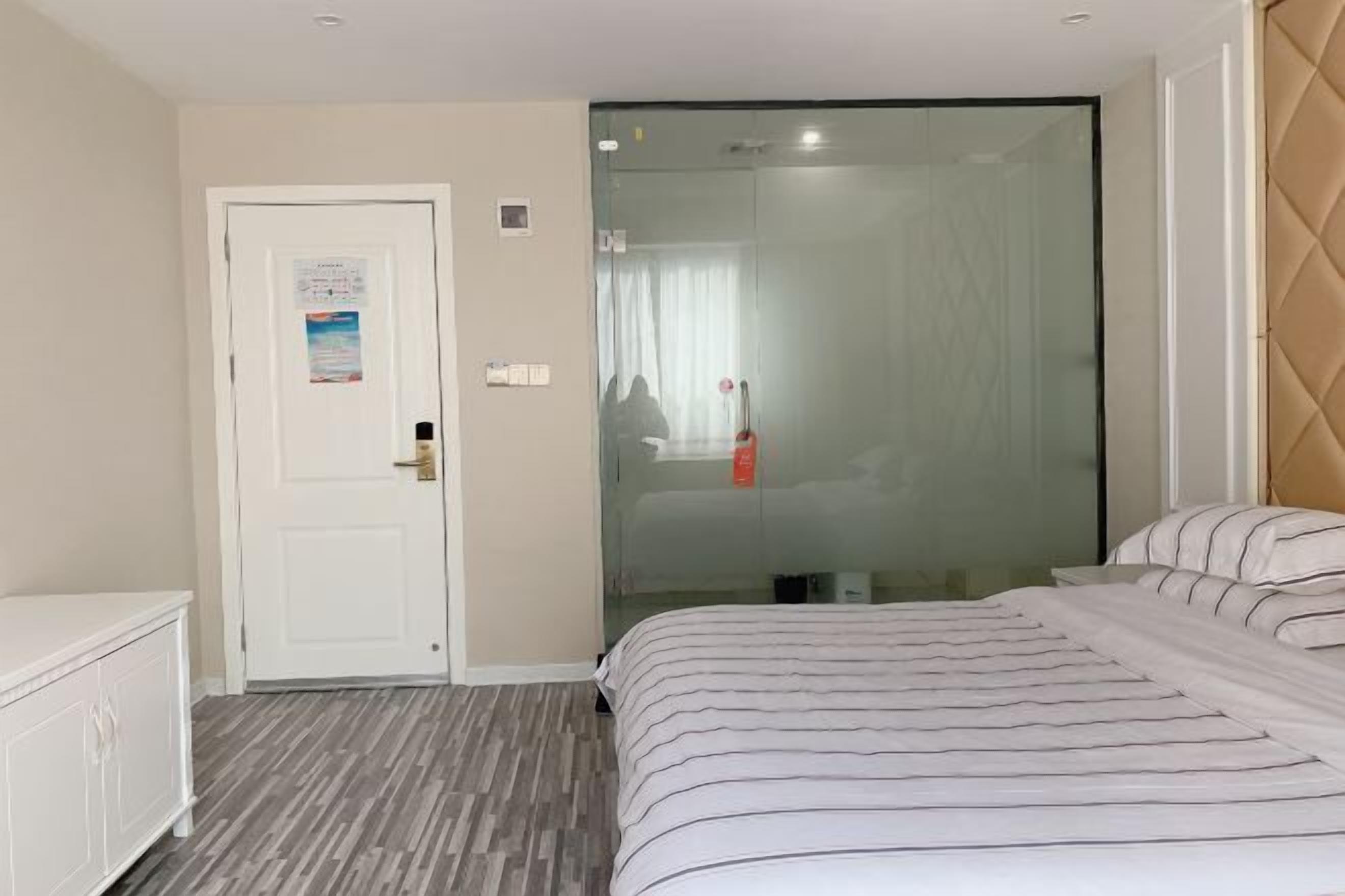 A hotel room with a bed, a white wardrobe, a door with a poster, and a glass shower enclosure.