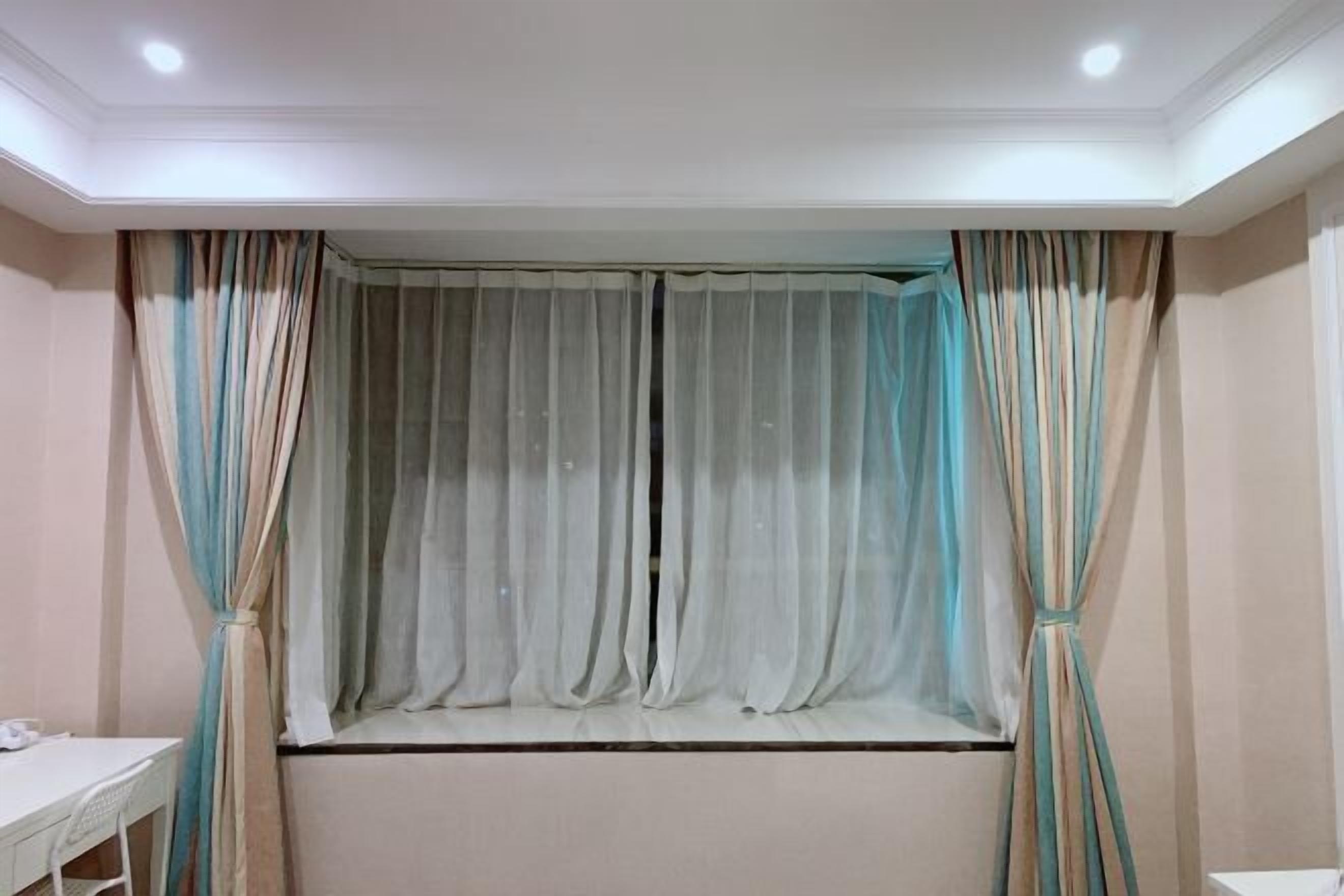 A room with a window covered by sheer curtains, a white desk, and a chair.
