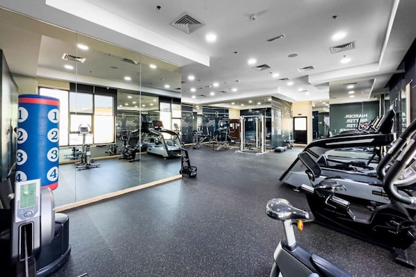 A modern gym with various exercise equipment, including treadmills and weight machines, and a mirrored wall.