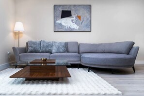 A modern living room with a grey sectional sofa, a glass coffee table, and a white shag rug.