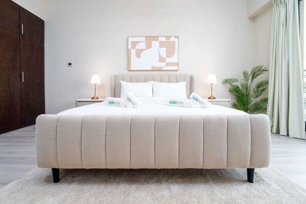 Una cama grande con edredón color beige, dos mesitas de noche con lámparas, una obra de arte abstracto en la pared y una planta en maceta.