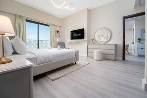 A modern bedroom with a bed, bedside table, lamp, TV, and a view of the balcony.