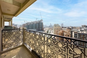 A balcony with intricate metal railings overlooking a cityscape with buildings and construction cranes.