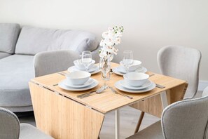 A dining table set with white plates, bowls, and cutlery, accompanied by a vase of white flowers.