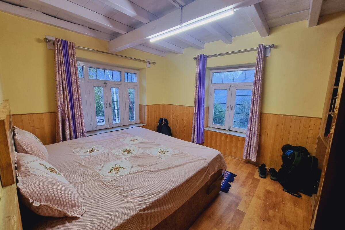 A bedroom with a bed, wooden walls, two windows with curtains, and a wooden floor.