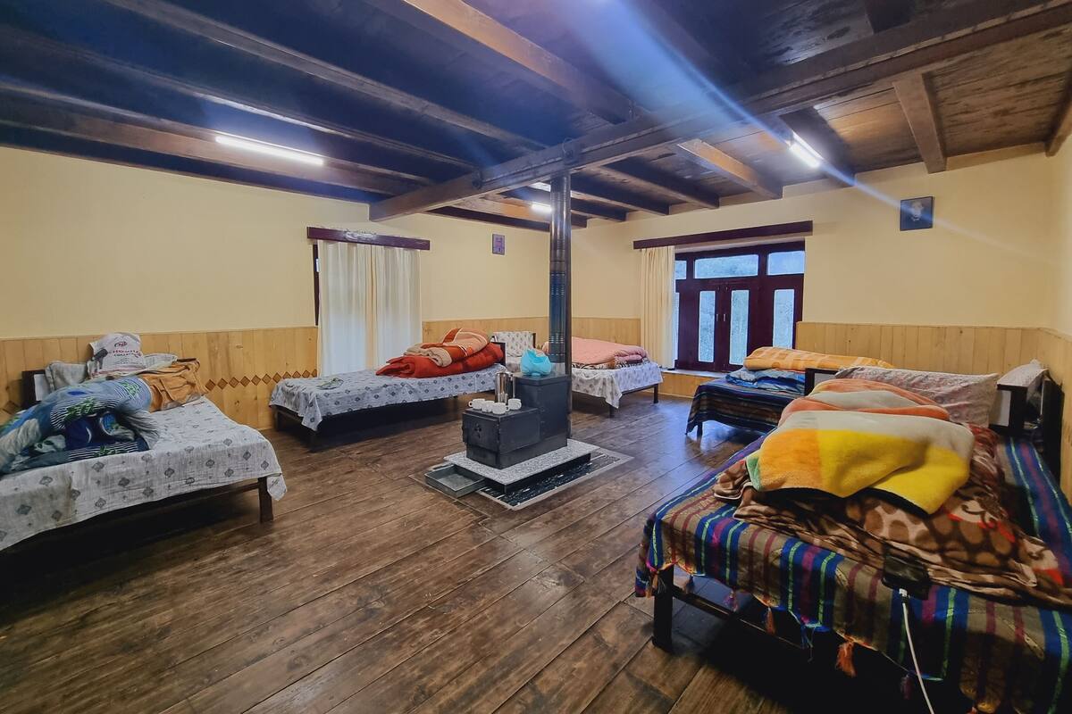 A rustic room with wooden floors, a central fireplace, and two beds with colorful bedding.
