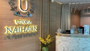 A reception area with a Utopia Naihar sign, a marble counter, a vase with yellow flowers, and a leather bench. - Mountainview Apartment in Naiharn (Rawai)
