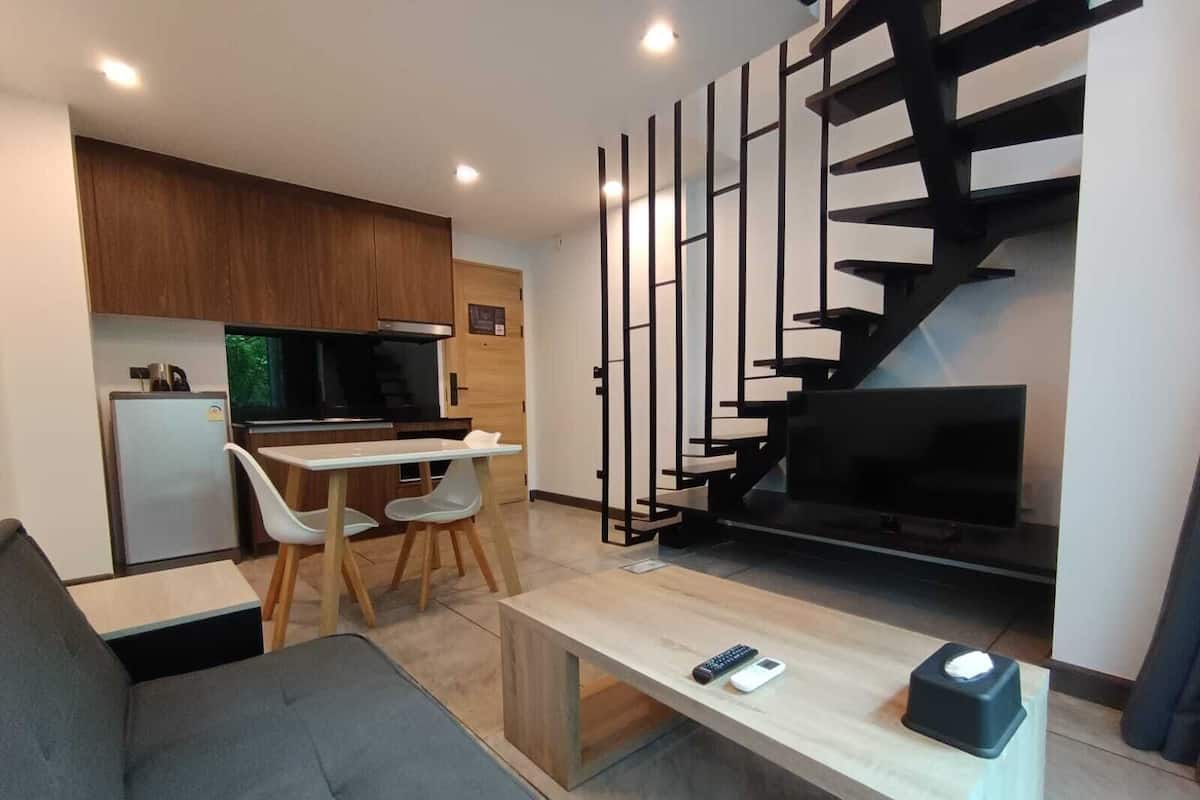 A modern living room with a sofa, a dining table with chairs, a TV, and a staircase.