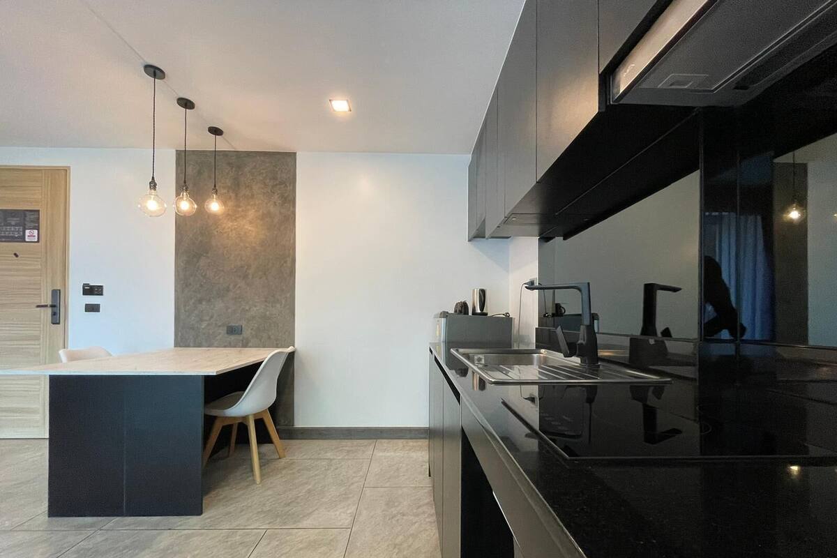 A modern kitchen with a black countertop, a built-in oven, and a sink. There is a wooden chair and a small dining table.