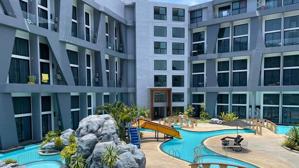 A modern hotel with multiple floors, a central swimming pool with a slide, and outdoor seating areas. - Mountainview Apartment in Naiharn (Rawai)