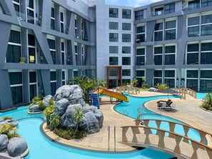A modern hotel with multiple floors, a central swimming pool with a slide, and outdoor seating areas. - Mountainview Apartment in Naiharn (Rawai)