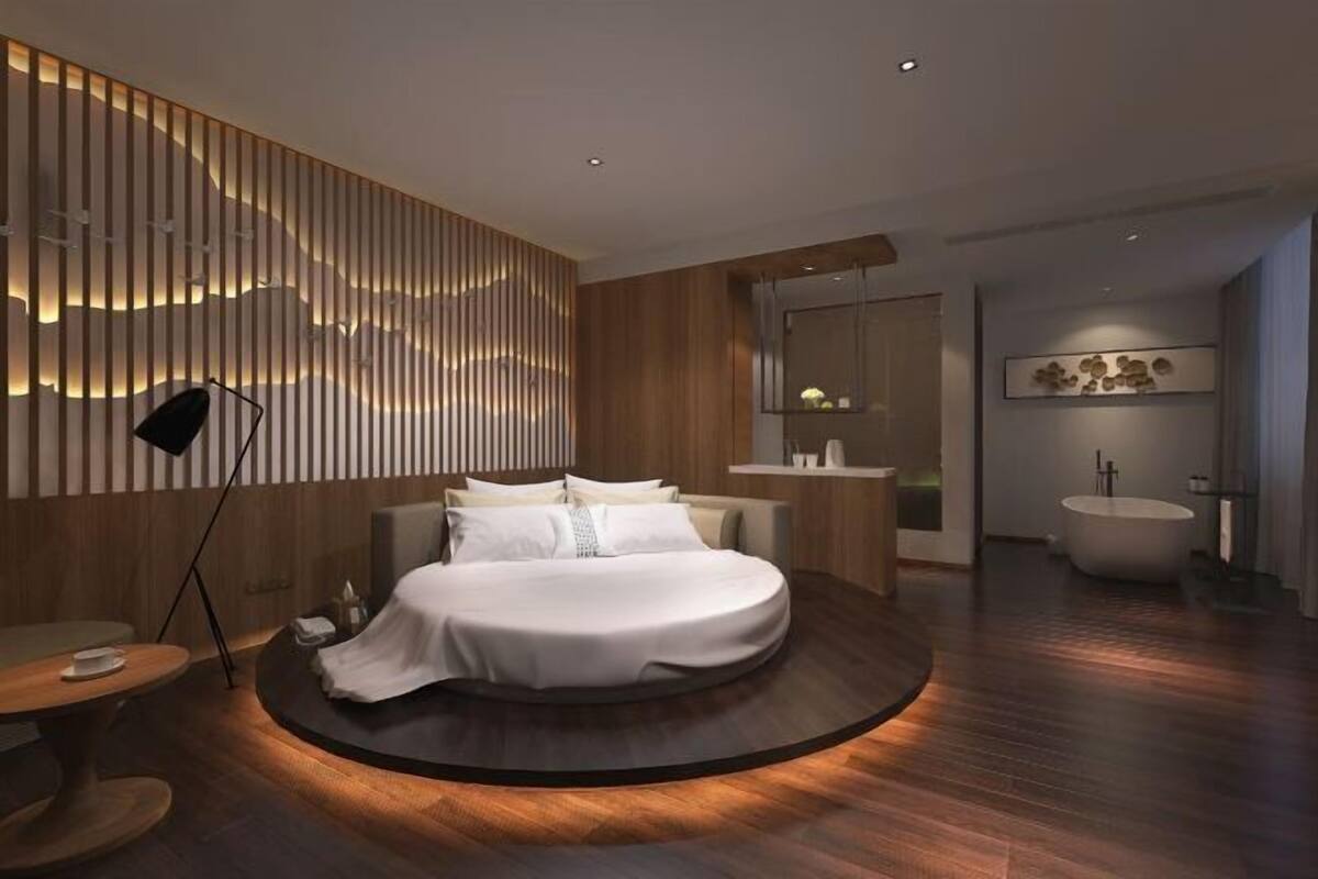 Een moderne slaapkamer met een rond bed, een houten paneelwand, een nachtkastje en een groot raam.