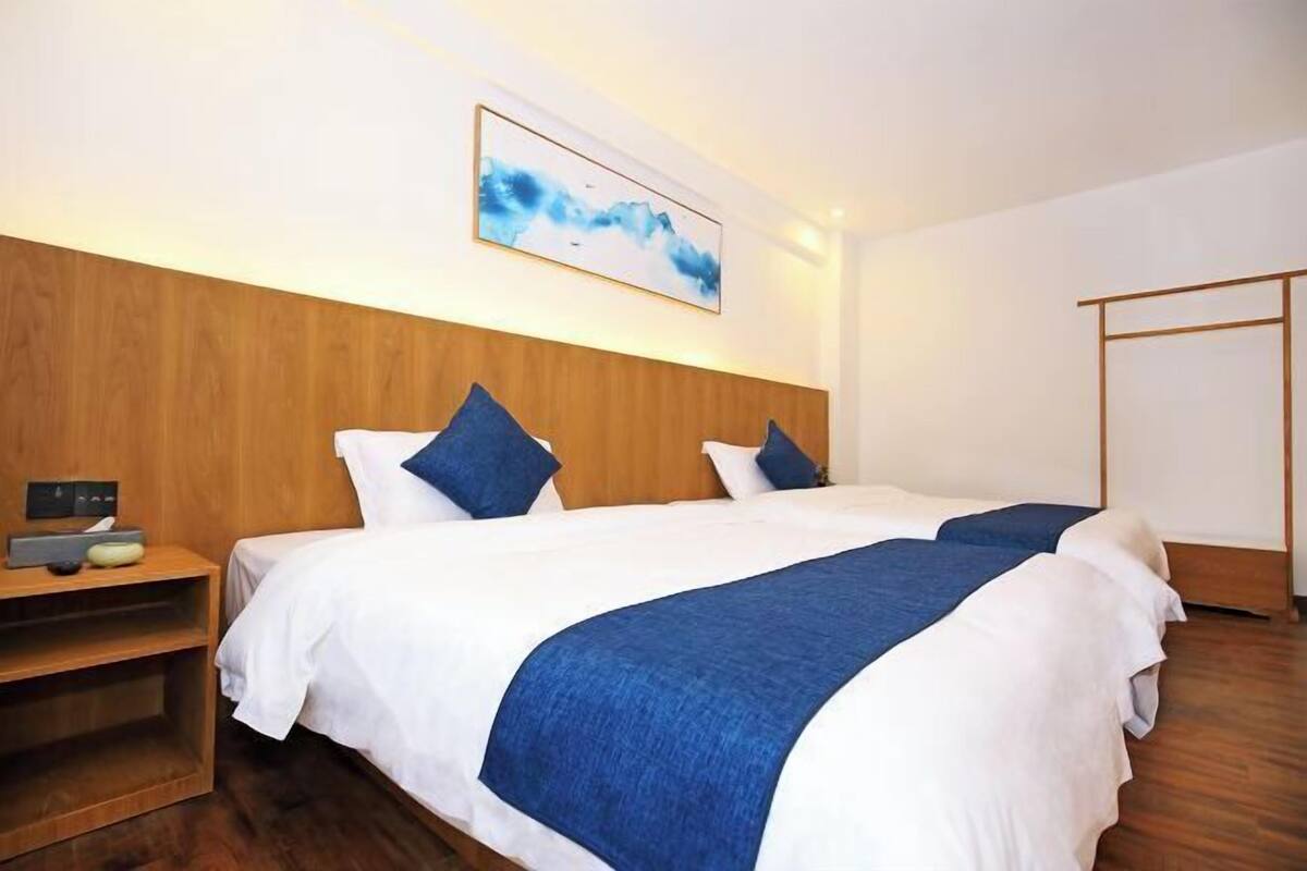 Een hotelkamer met een houten hoofdbord, een bed met wit- en blauwe beddengoed, een nachtkastje en een aan de muur hangend kunstwerk.