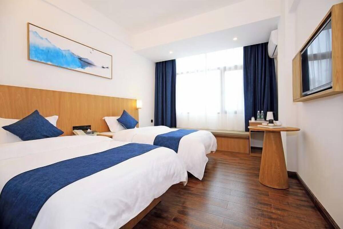 Hotelkamer met twee bedden, een houten hoofdbord, een nachtkastje, een televisie en een raam met gordijnen.