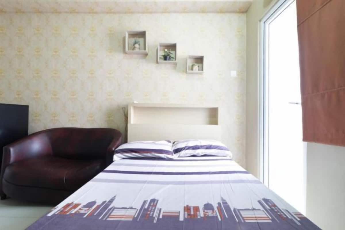 Ein Schlafzimmer mit einem Bett, einem braunen Ledersessel, einem weißen Nachttisch und einem Fenster mit brauner Jalousie.