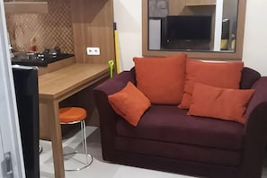 A living area with a sofa, a dining table, and a kitchen area. - Green Pramuka City by SR Property (Central Jakarta)
