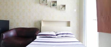 Quarto com cama, uma cadeira, mesa de cabeceira e janela.