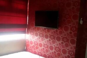 Une chambre avec un lit, un téléviseur fixé au mur et un papier peint à motifs.