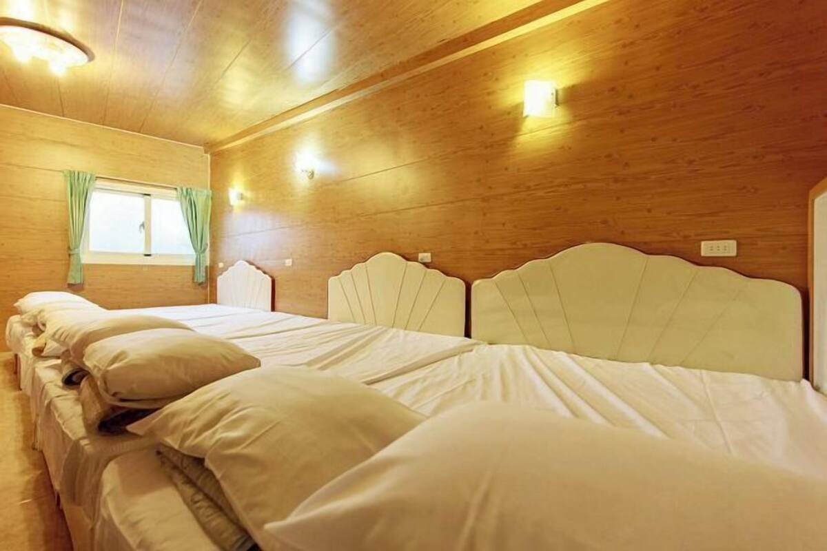 A room with wooden walls, a bed with white bedding, a window with curtains, and wall-mounted lights.