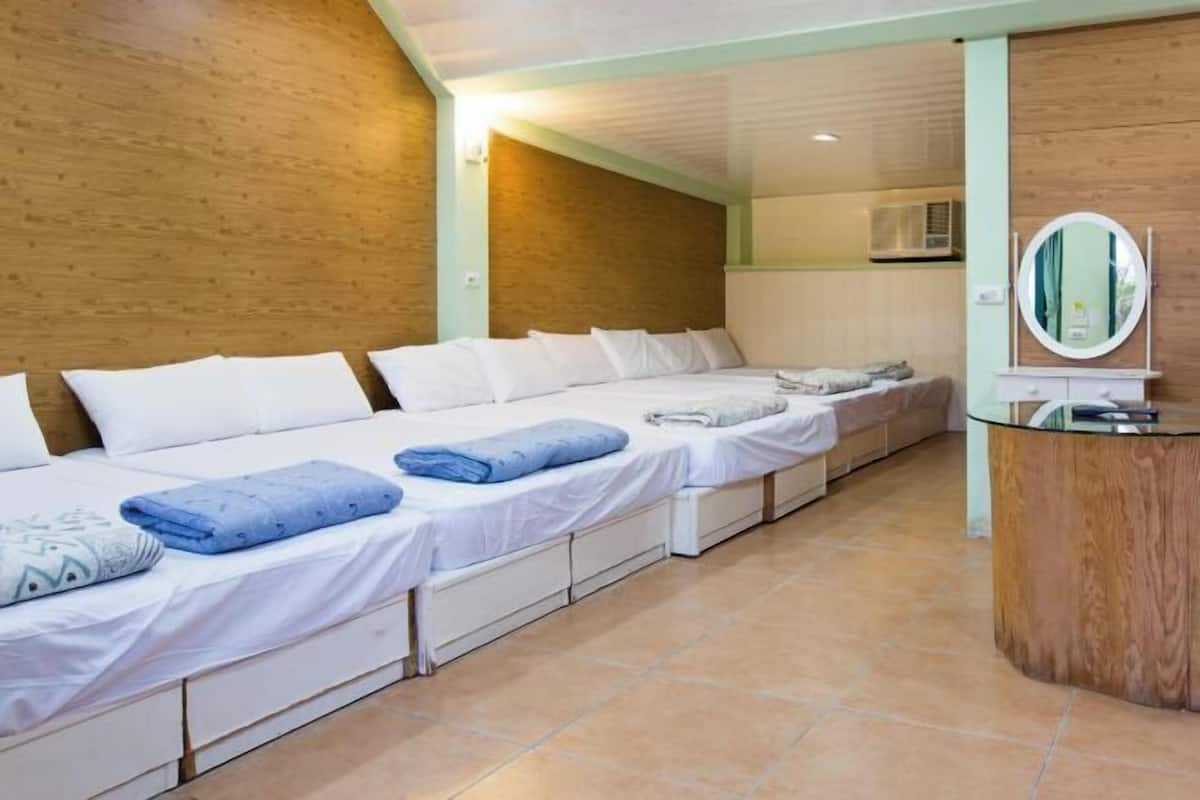 A hotel room with a long bed, a small bathroom, and a round mirror.