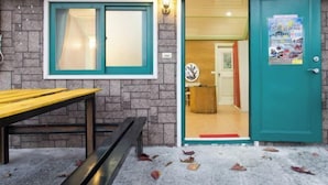 Une pièce avec une porte de couleur turquoise, un banc en bois et une fenêtre dont le cadre est également turquoise.