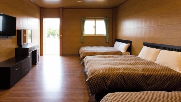 Une chambre d’hôtel avec des murs et un plancher en bois, un téléviseur à écran plat posé sur une commode, deux lits avec une literie à motifs et une fenêtre avec des rideaux.